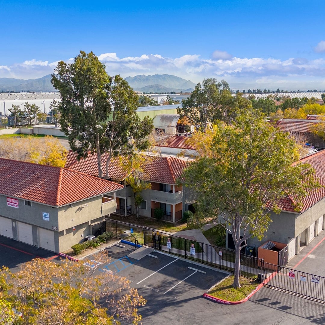 Aerial view of Cambria Villas multifamily residential community in Rialto, California, featuring Spanish-style red tile roofs, gated entrance, parking lot and mountain backdrop