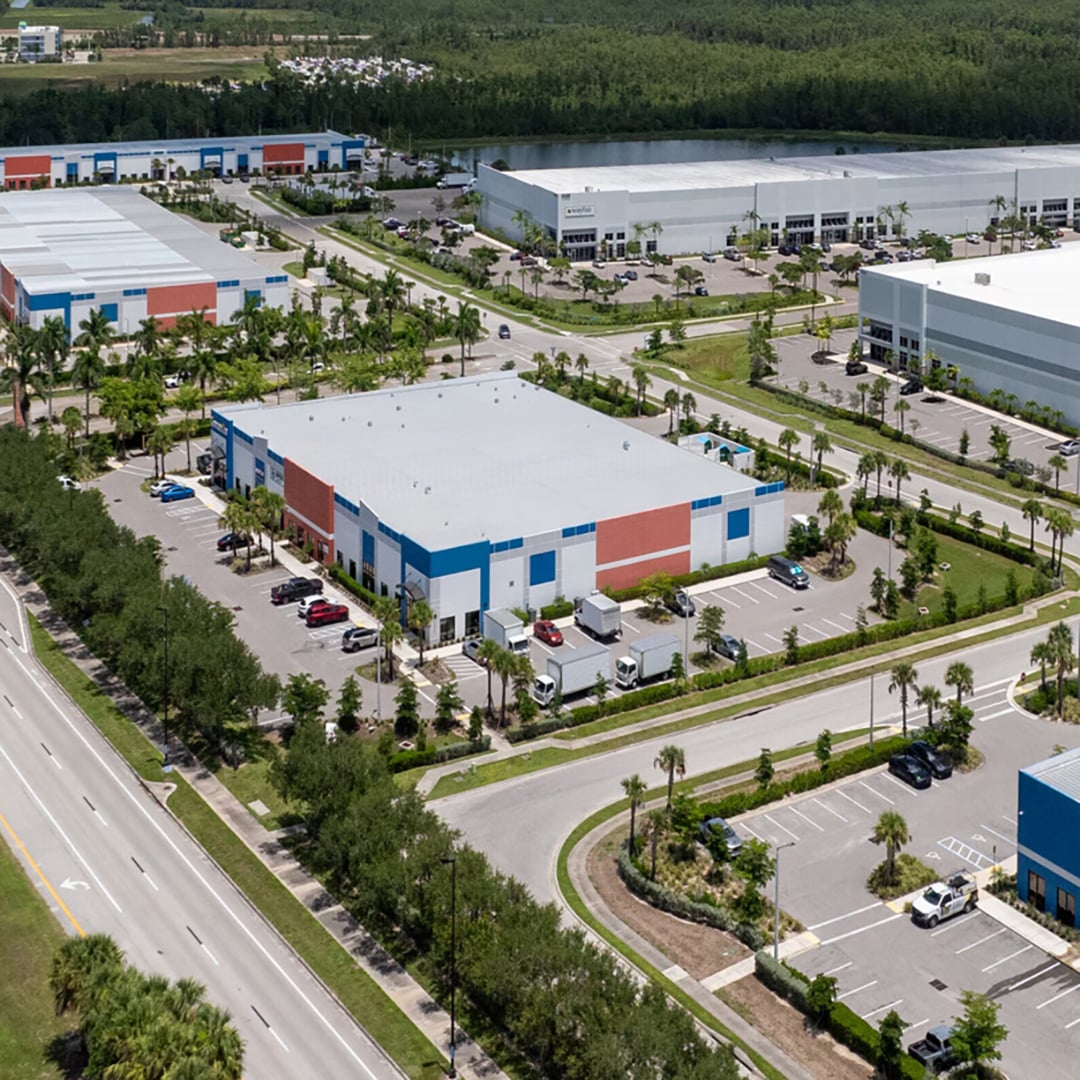 Aerial view of Meridian business park featuring multi-tenant industrial warehouse buildings with blue and red facades, palm tree-lined streets, and truck loading areas in a Florida suburban setting