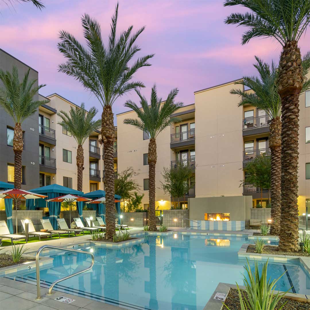 Resort-style pool at Broadstone Seventh multifamily community in Phoenix AZ featuring cabanas, fire pit, palm trees, and illuminated buildings at dusk