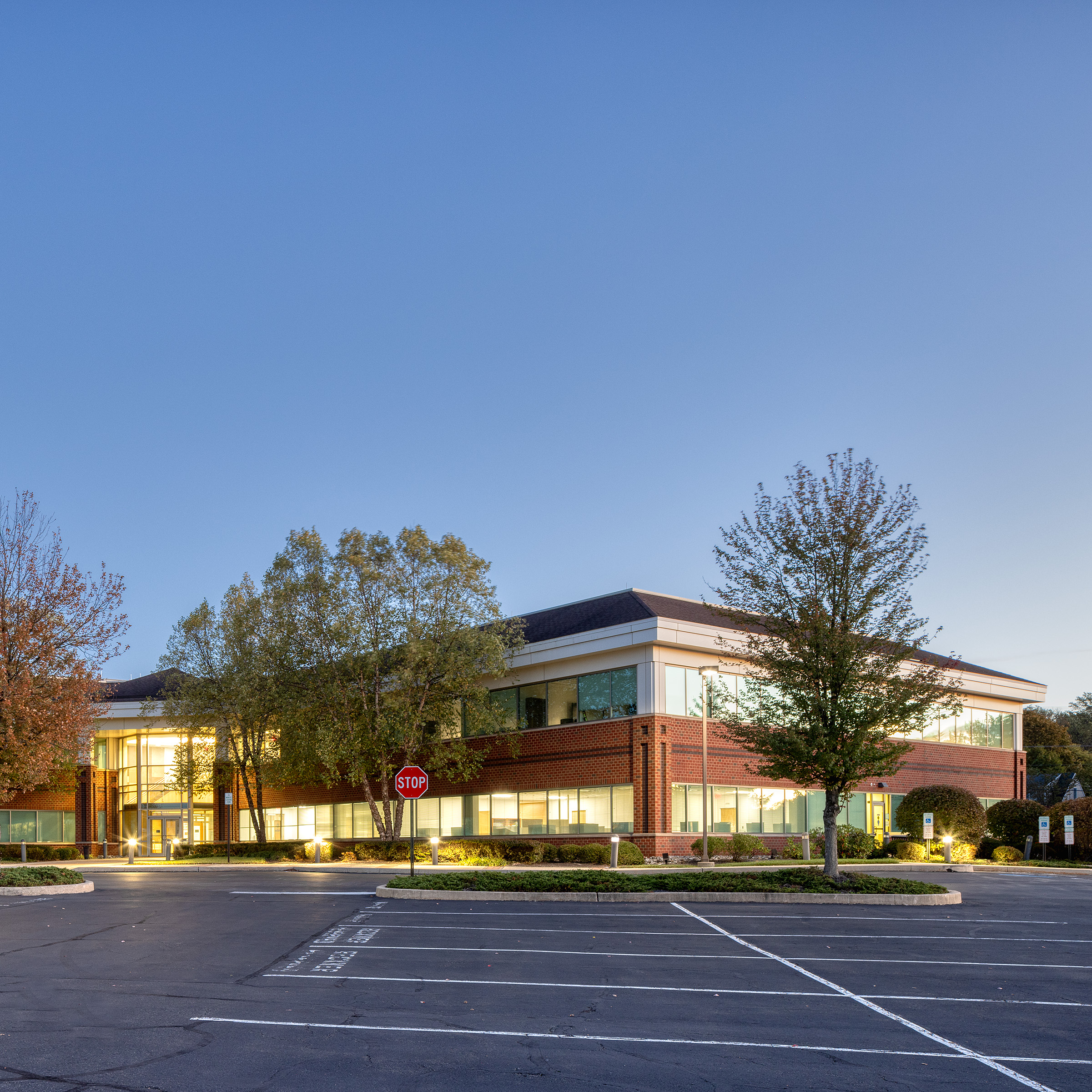 Exterior dusk photo of 1600 Manor Drive, a two-story brick and glass commercial office building with illuminated windows and landscaped parking lot.