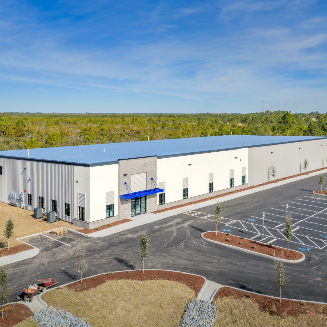 Aerial view of 8388 Water Tower, a newly constructed industrial flex warehouse building with blue canopy entry, fresh parking lot, and wooded backdrop.