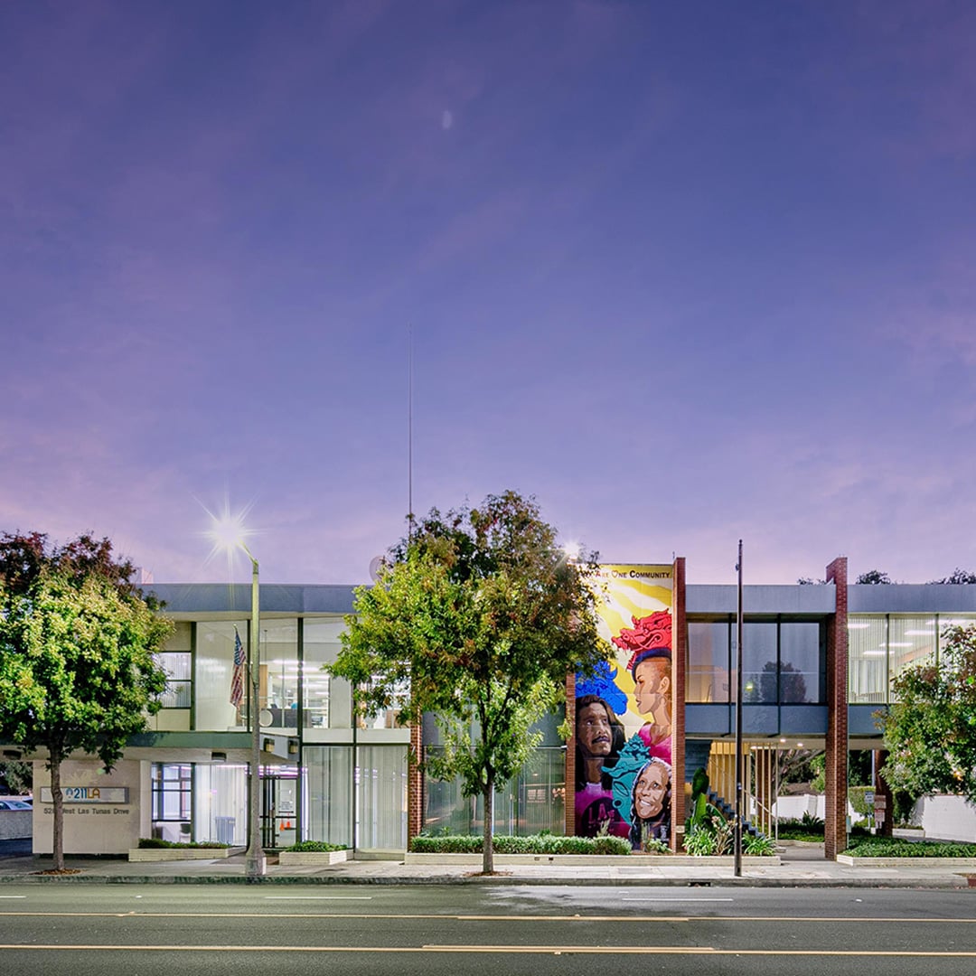 Twilight exterior of 526 W Las Tunas Drive office building in San Gabriel, CA featuring a colorful community mural, glass facade, and illuminated interiors.