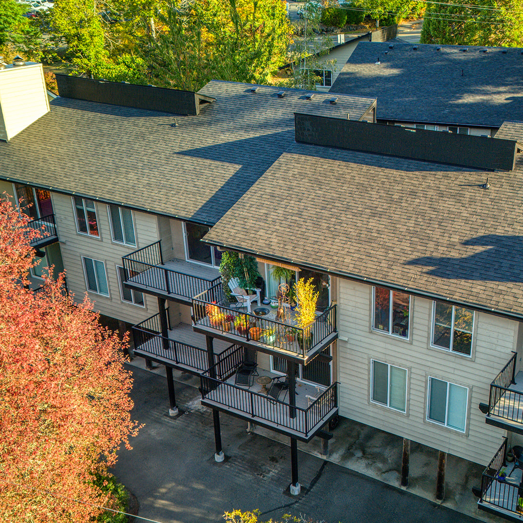 Aerial view of a multifamily apartment building with stacked private balconies, shake rooflines, and surrounding autumn foliage in red and gold
