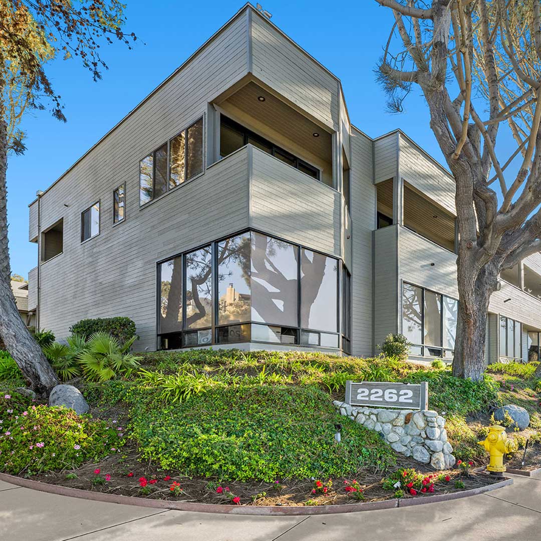 2262 Carmel Valley Road Del Mar CA industrial office building with floor-to-ceiling corner windows, stone address sign, and lush drought-tolerant landscaping
