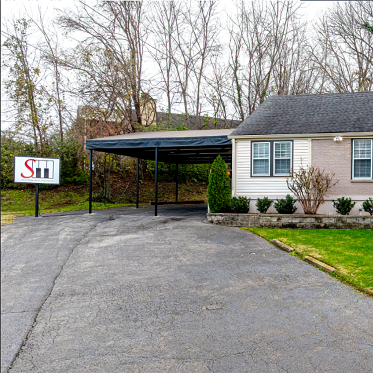Exterior view of a 1,650 square foot single-story brick office building at 2700 Lamon Avenue featuring a carport, manicured landscaping with evergreen shrubs, and a raised stone retaining wall along a curved driveway