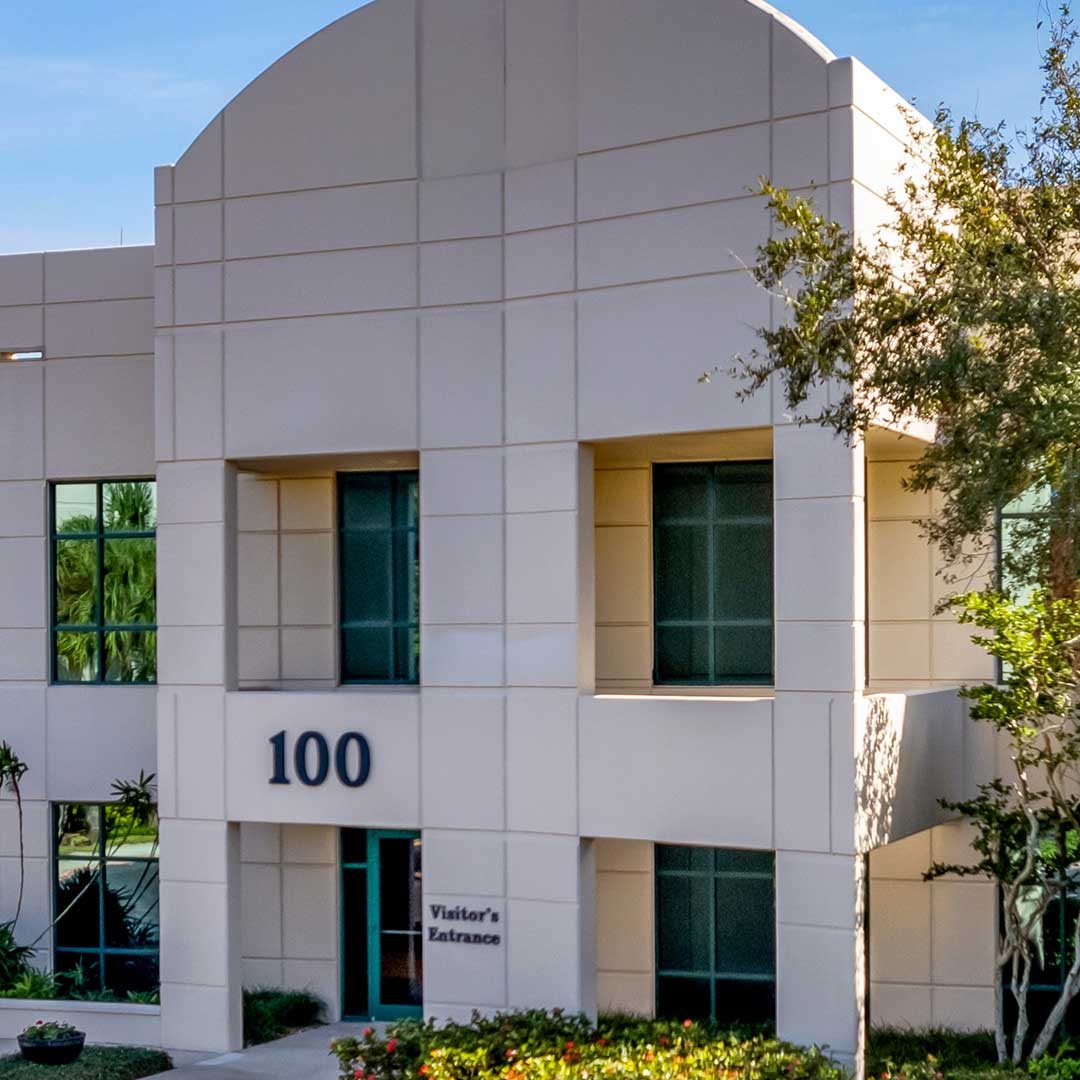 Exterior of modern medical office building with visitor entrance signage and suite number 100, surrounded by landscaping in a commercial property setting.