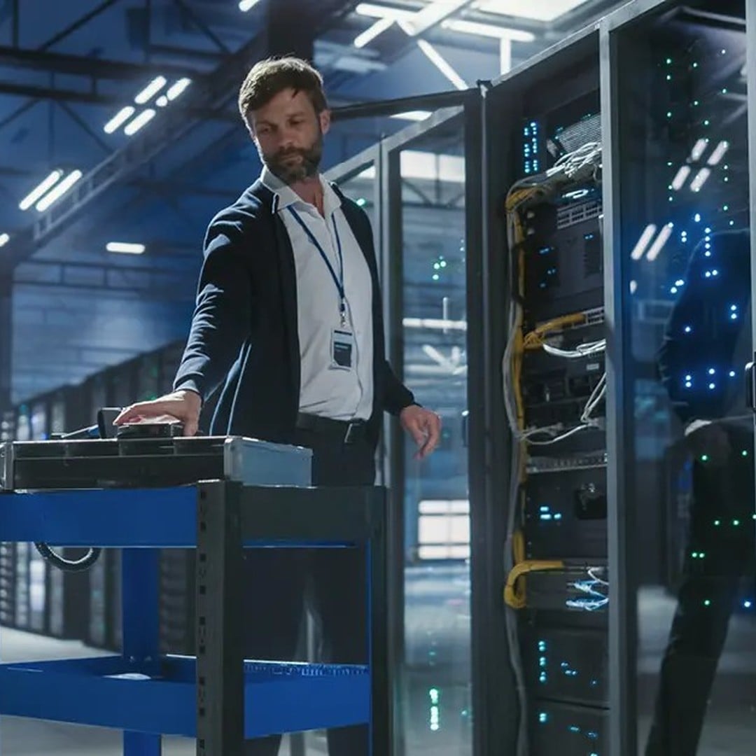 An IT technician works among server racks in a data center facility, illustrating the growing demand for data center space amid global supply constraints.
