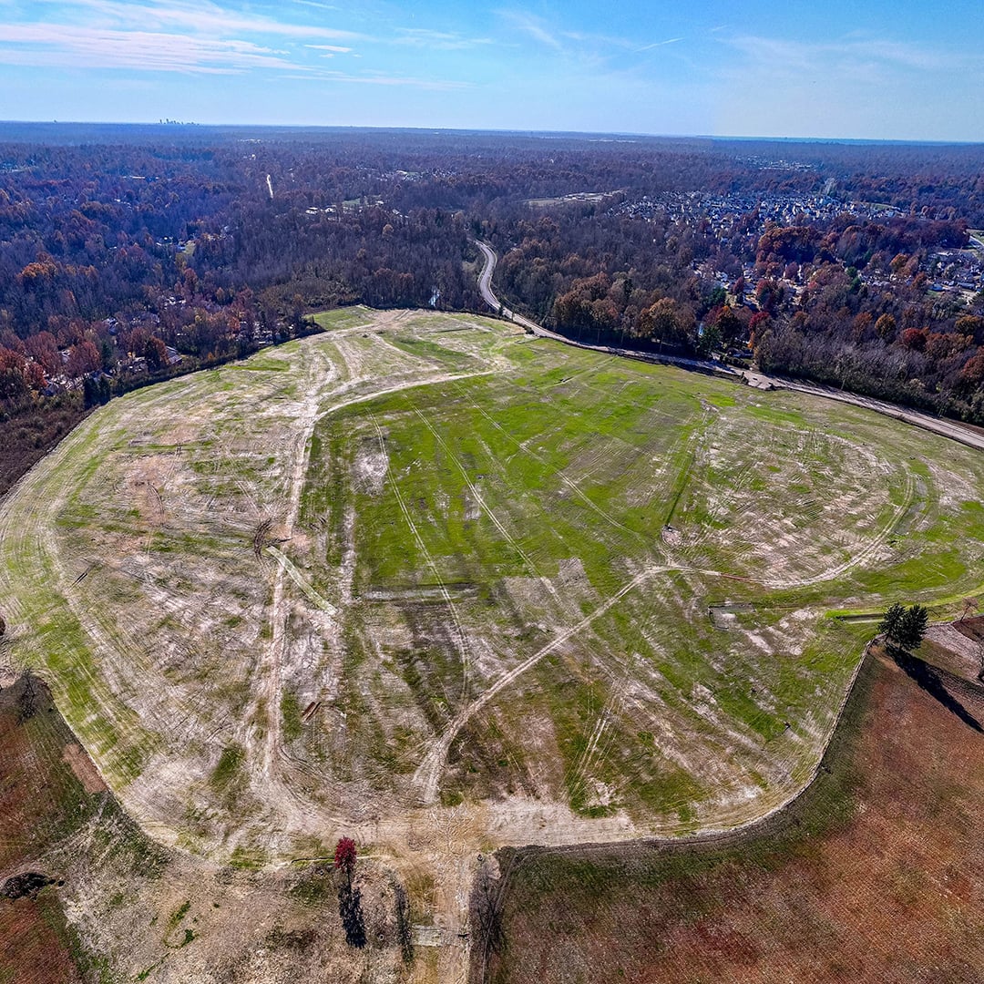 Aerial view of a large cleared vacant land parcel surrounded by trees, suitable for commercial or mixed‑use development.