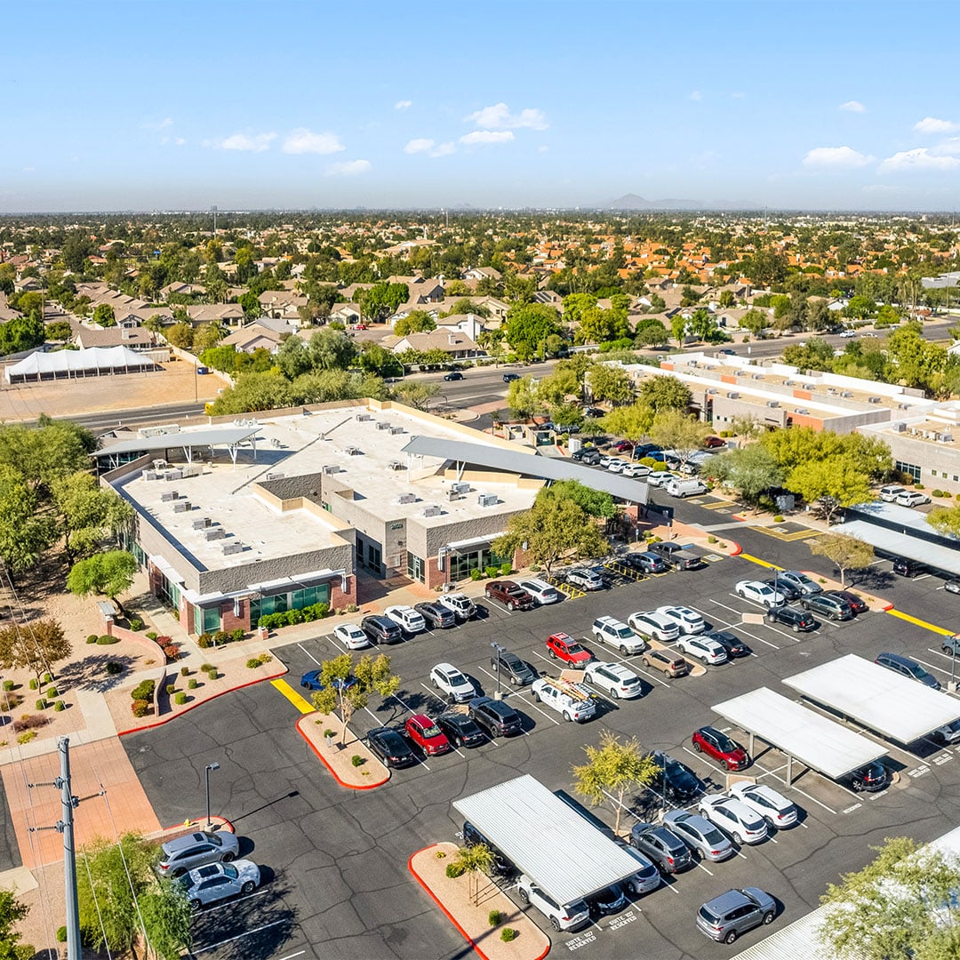 Aerial view of a suburban retail center with surface and covered parking surrounded by residential neighborhoods in Gilbert, Arizona.
