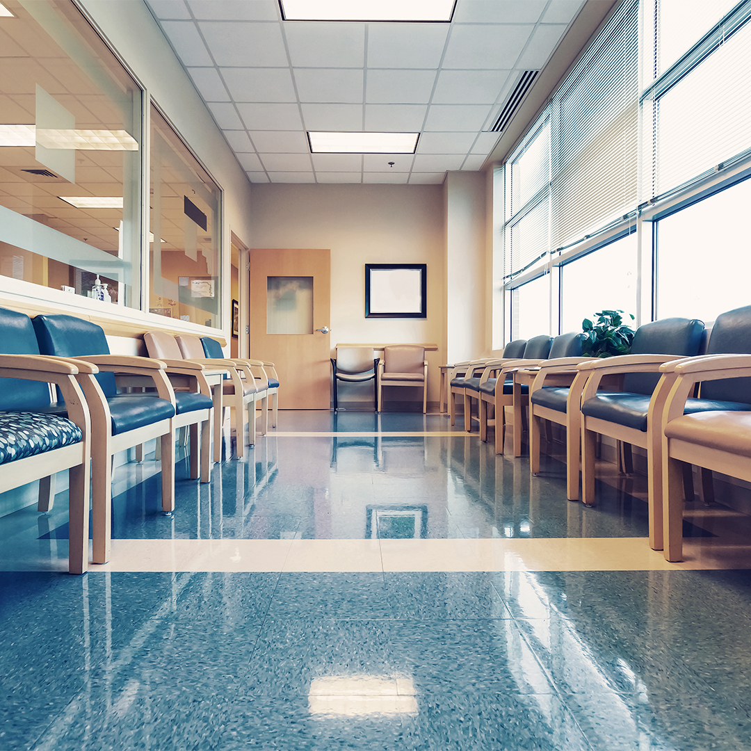 Empty medical office waiting room with rows of chairs, polished floors, and daylight from windows in a healthcare clinic.