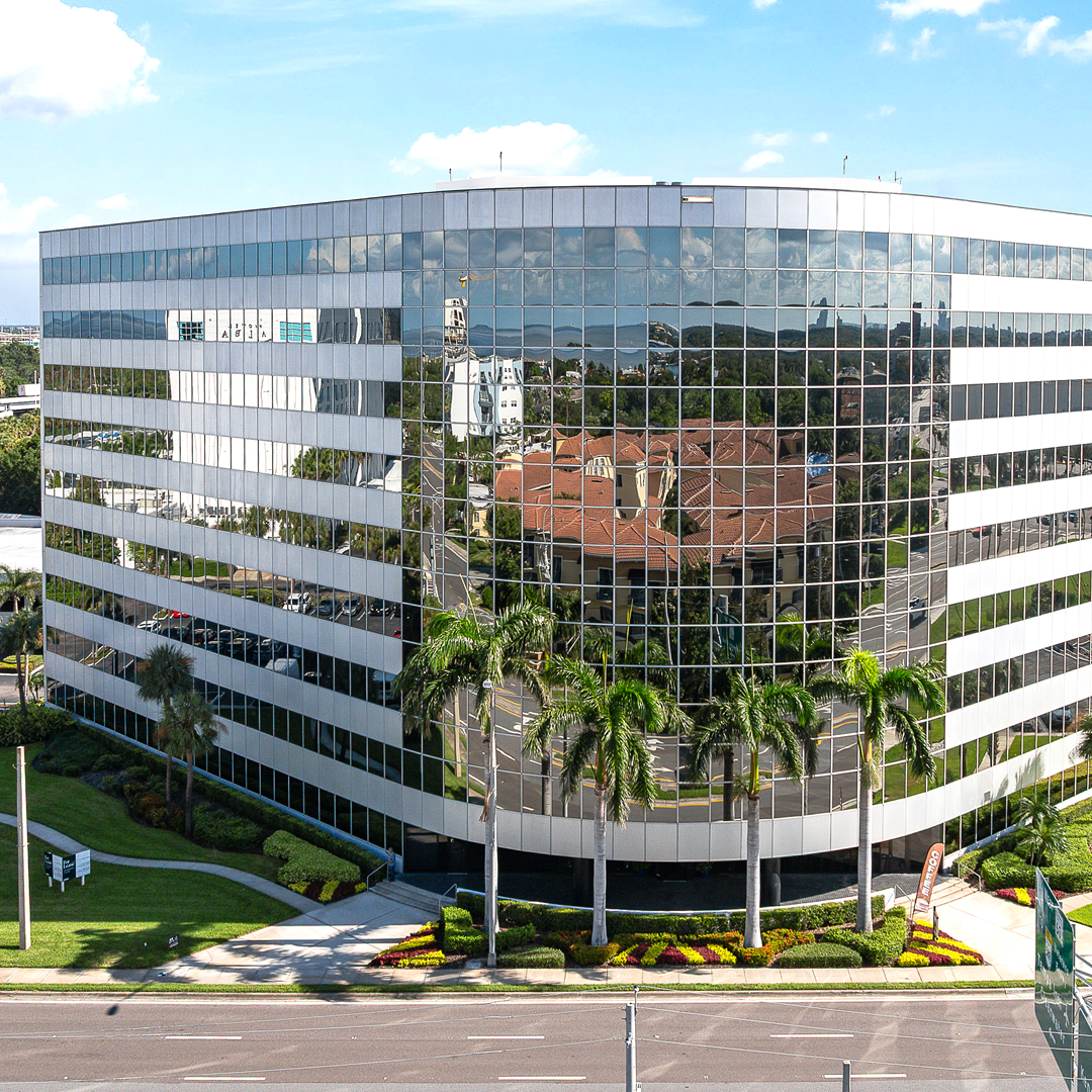 Aerial view of the Bridgeport office building featuring reflective glass exterior, landscaped grounds, and palm trees along a commercial roadway.