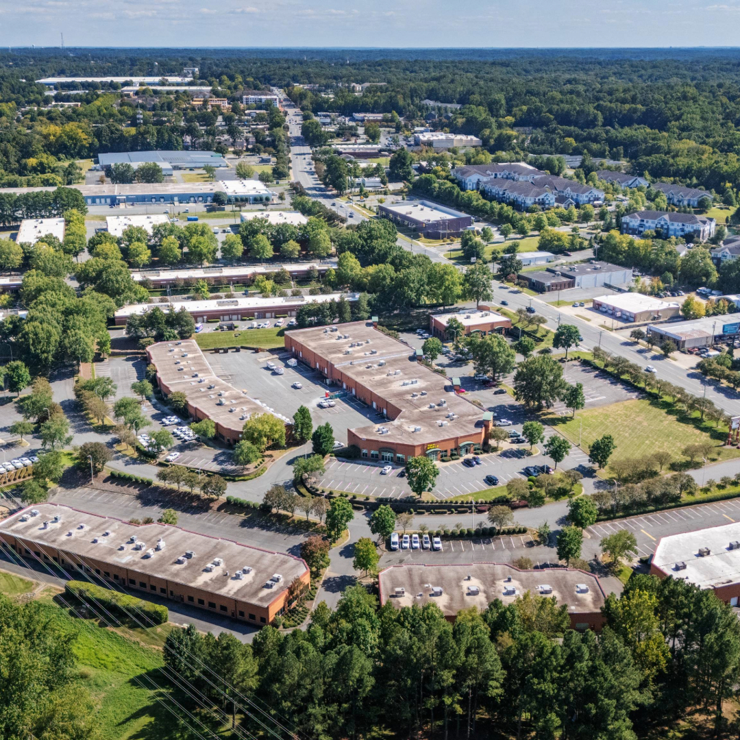 Aerial view of a suburban commercial office park with multiple low-rise buildings, surface parking, and landscaped green space.