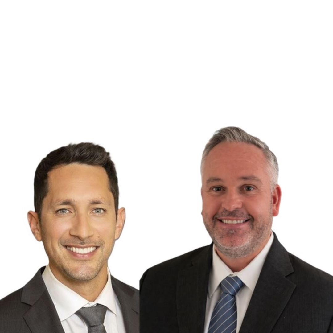 A clean, professional image showcasing two team members in formal business attire on a white background.