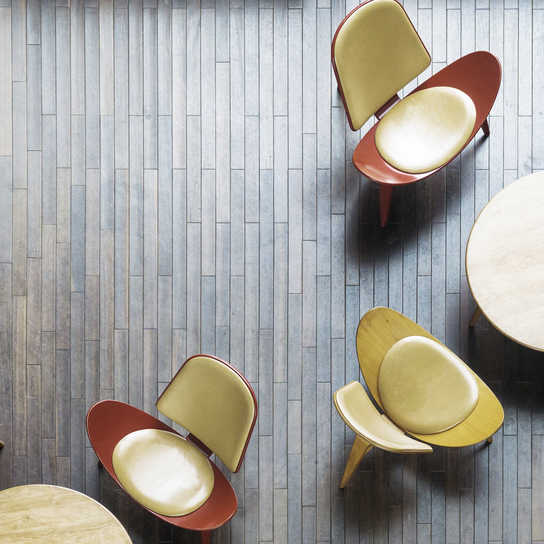 Aerial view of a modern office lobby featuring small tables, contemporary chairs, and wood plank flooring in a shared seating area.
