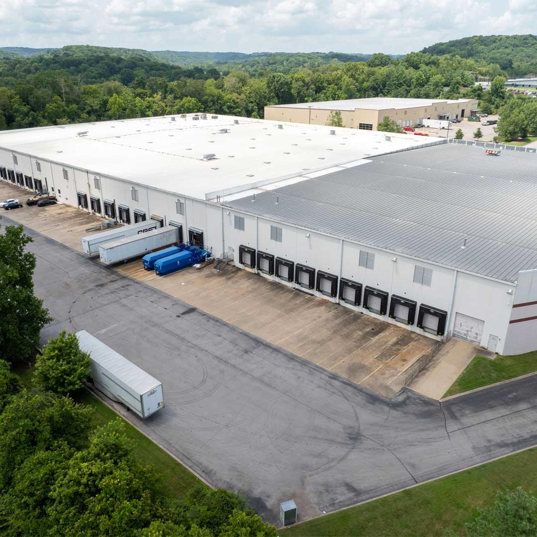 Aerial view of a large industrial warehouse facility with multiple loading docks and truck access surrounded by greenery.