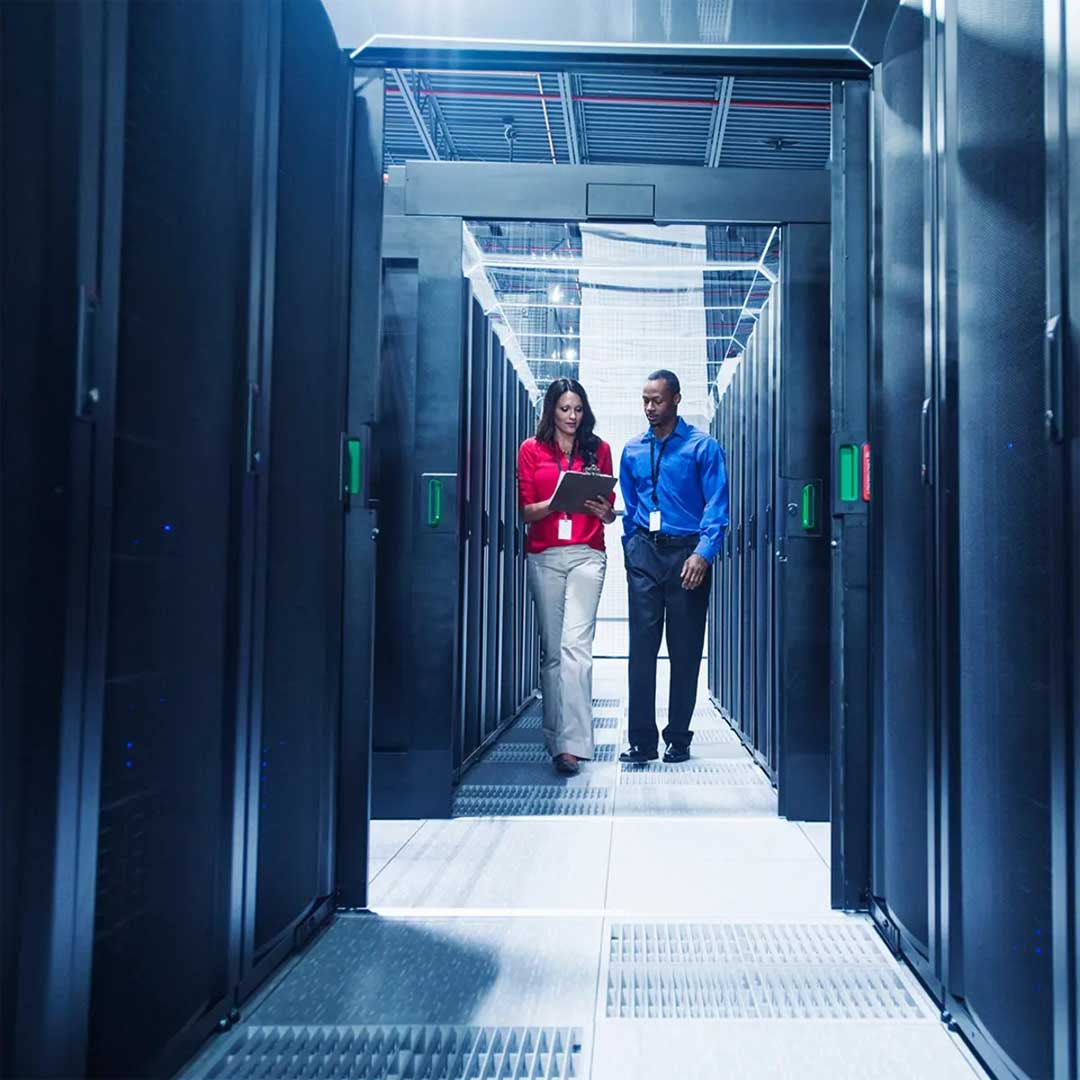 Professionals walking through a data center aisle with server racks, representing Washington State’s growth in data center leasing.