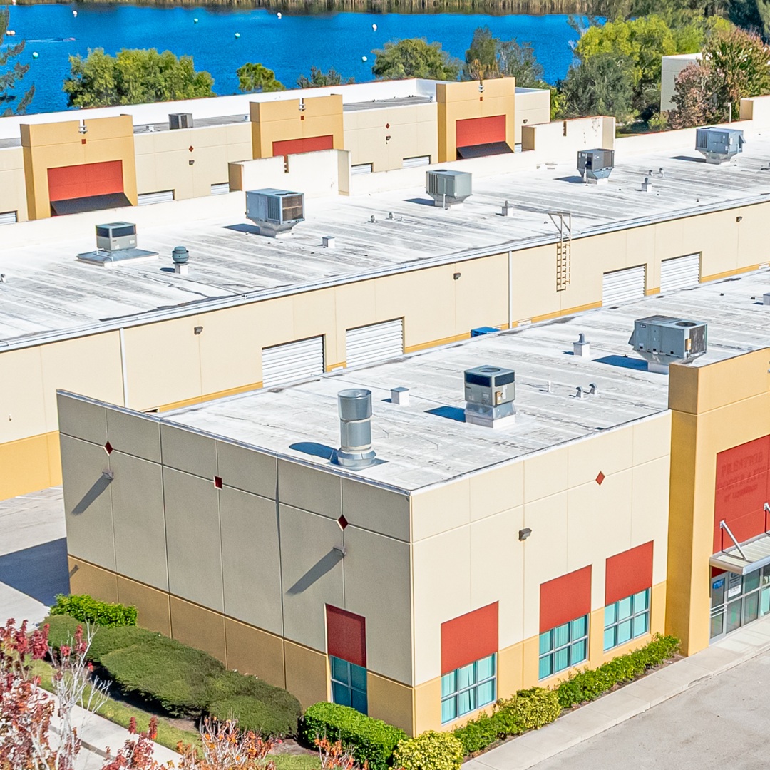 Aerial view of light industrial warehouse buildings with roll up loading doors and rooftop units near a waterfront