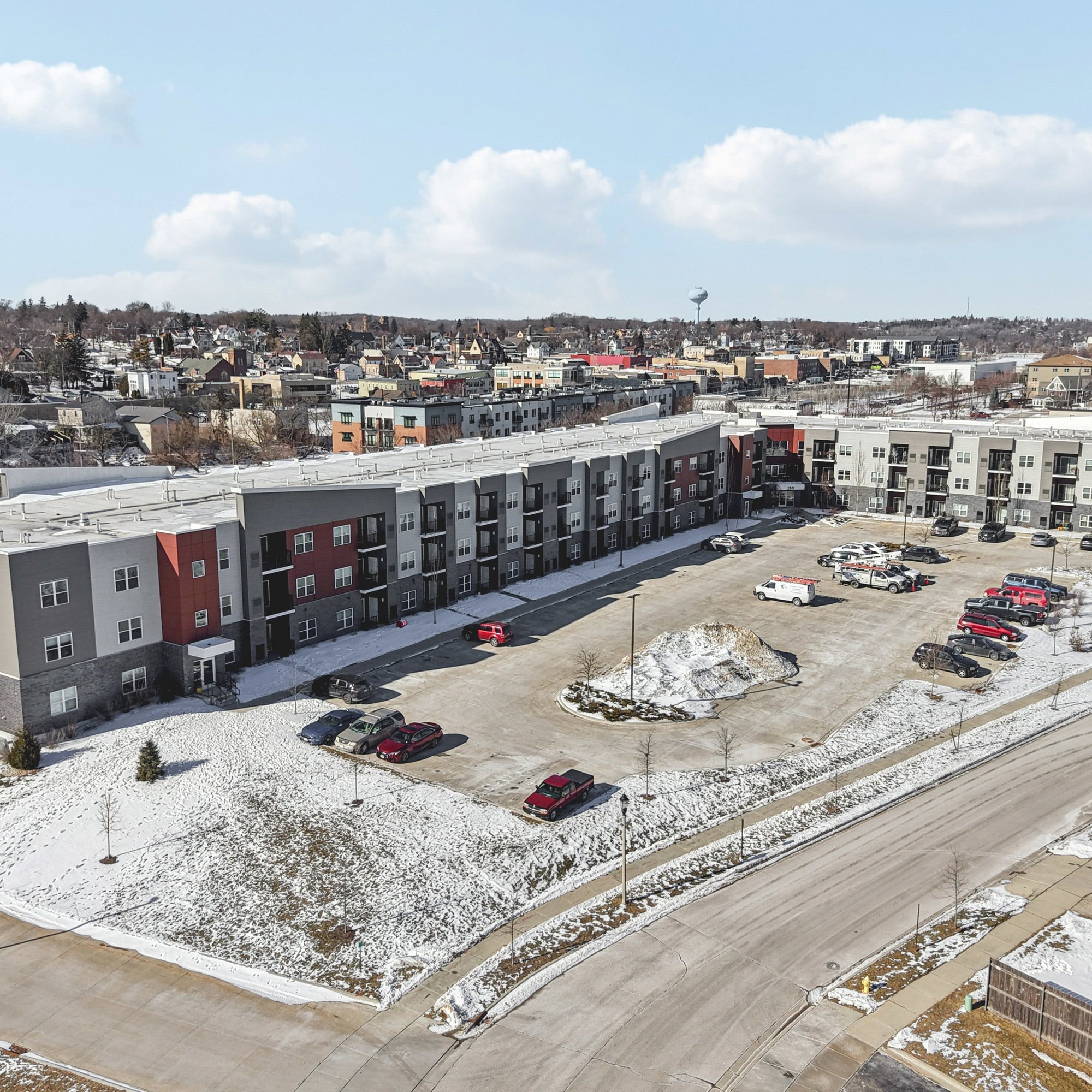 Aerial view of a modern multifamily apartment complex with surface parking lot in a snow-covered suburban neighborhood