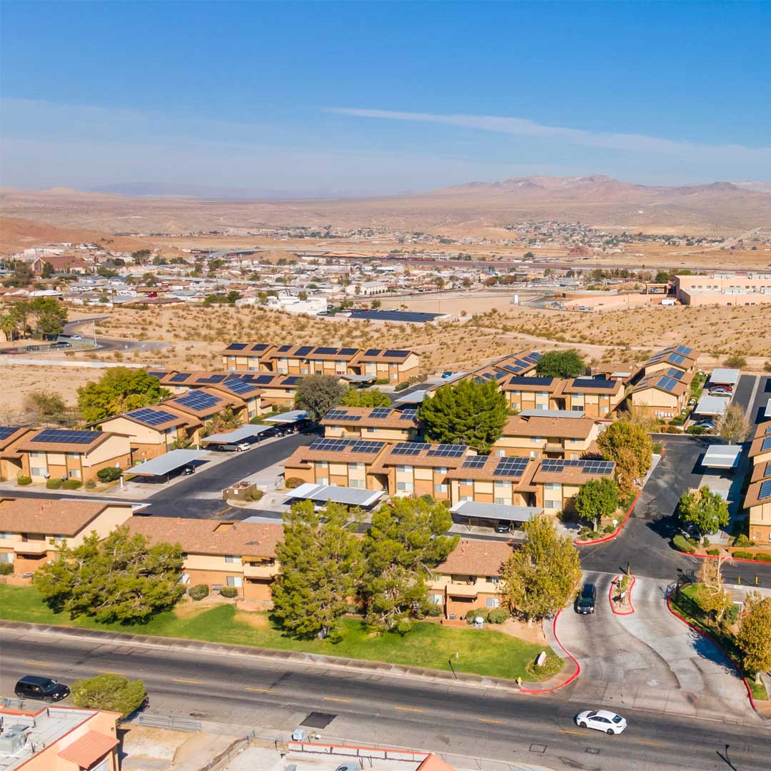 Aerial view of Sunrise Vista Apartments with solar panels, desert landscape, and mountain backdrop in a sunny Southwest community.