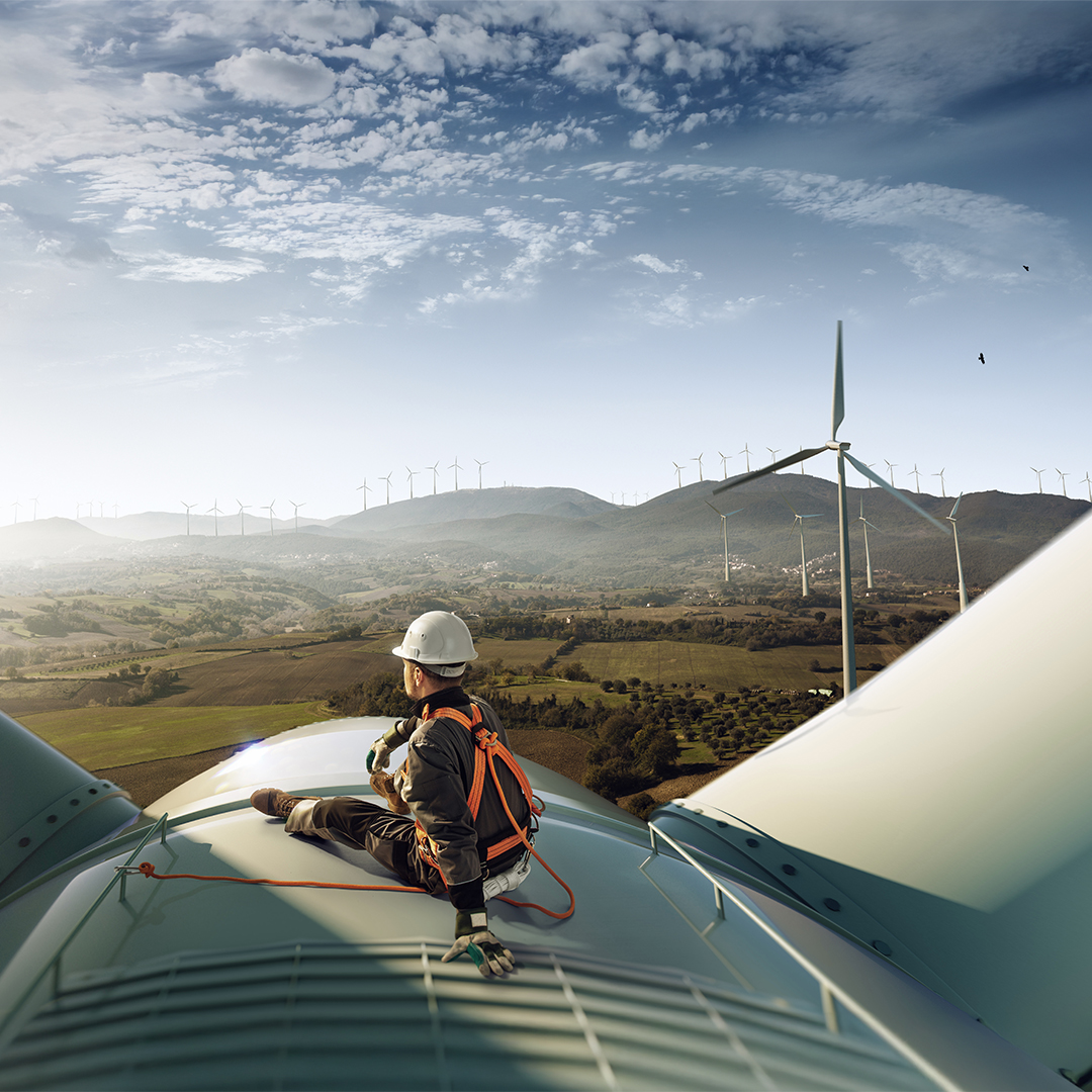 worker sits on top of a wind energy generator