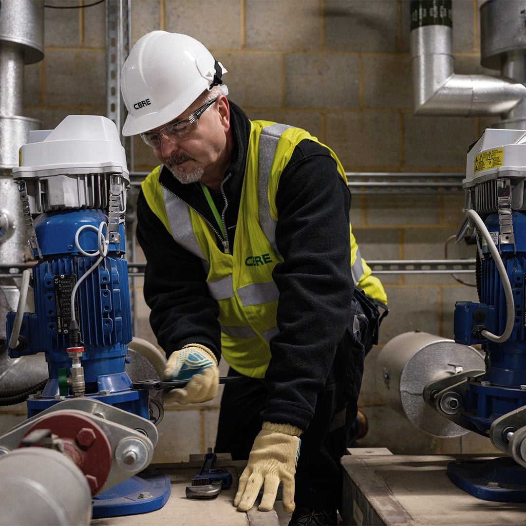 Technician wearing safety gear adjusts industrial pump equipment inside a mechanical room.