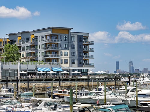 Exterior of Meriel Marina Bay luxury waterfront apartment community overlooking a marina with boats and city skyline visible in the background.
