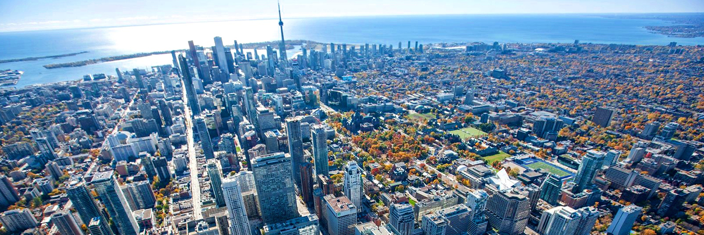 Aerial view of downtown Toronto and the CN Tower, with autumn foliage and Lake Ontario beyond, showcasing the city’s commercial core.
