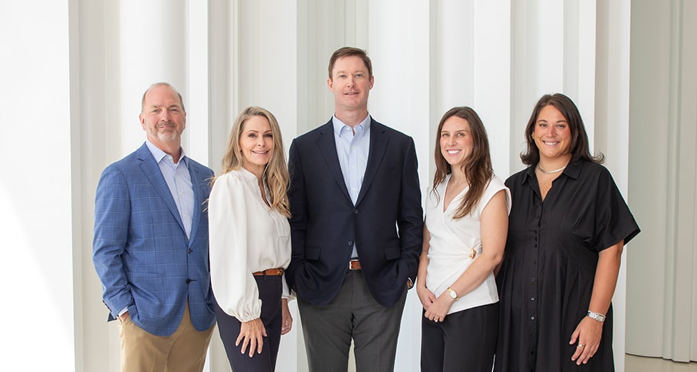 Professional group portrait of five commercial real estate team members in business attire posed against a white architectural column backdrop.