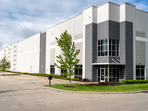 Exterior view of a modern industrial warehouse with glass office entry, clean façade design, and landscaped surroundings.