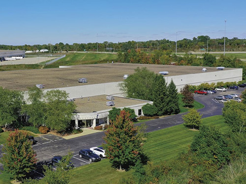 Aerial view of the industrial building at 675 Mondial with landscaped grounds and adjacent parking lot.