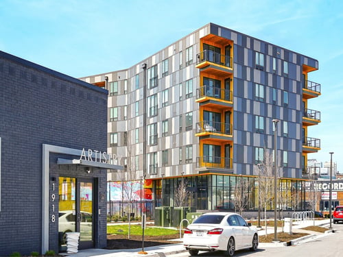 Artistry apartment building exterior at 1918 featuring a modern multi-story residential tower with orange and grey panel facade, balconies, and ground-floor entry