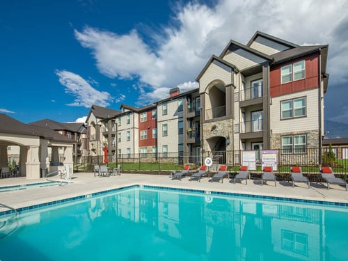 Eversage apartment community outdoor resort-style swimming pool with lounge chairs, mountain backdrop, and multi-story residential buildings under blue sky