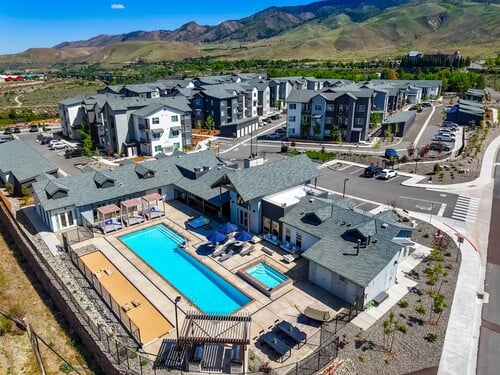 Aerial view of The Kallan apartment community featuring a resort-style pool with sun deck, modern residential buildings, and dramatic Nevada mountain backdrop
