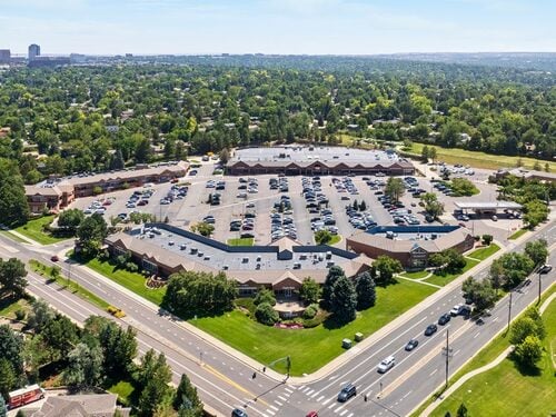 Aerial view of The Orchards suburban retail shopping center with large surface parking lot, brick commercial buildings, and mature tree-lined Denver neighborhood