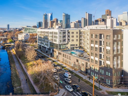 Aerial view of TriVista on Speer apartment community along Cherry Creek with rooftop pool amenity and downtown Denver skyline in the background