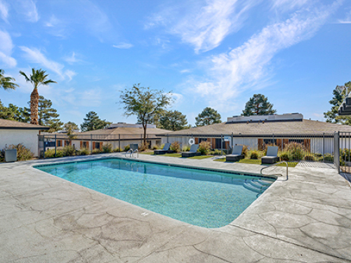 Outdoor swimming pool with lounge chairs at a multifamily apartment community, surrounded by landscaped grounds and residential buildings.