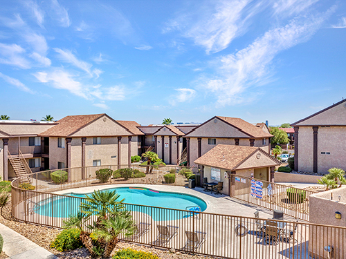 Outdoor swimming pool within a garden-style apartment community courtyard, surrounded by two-story residential buildings and landscaped grounds.