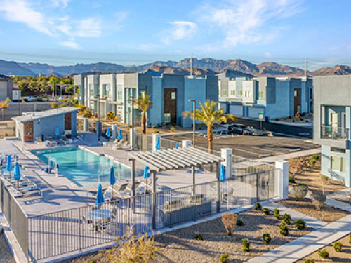 Modern apartment community featuring a resort-style outdoor pool, contemporary buildings, palm trees, and mountain views.