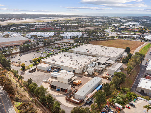 An aerial view of an industrial and office complex surrounded by parking areas and nearby commercial development.