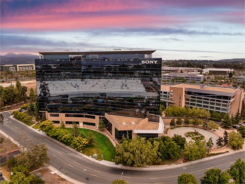 A sleek glass-and-stone corporate office building situated along a curved road with landscaped surroundings at dusk.