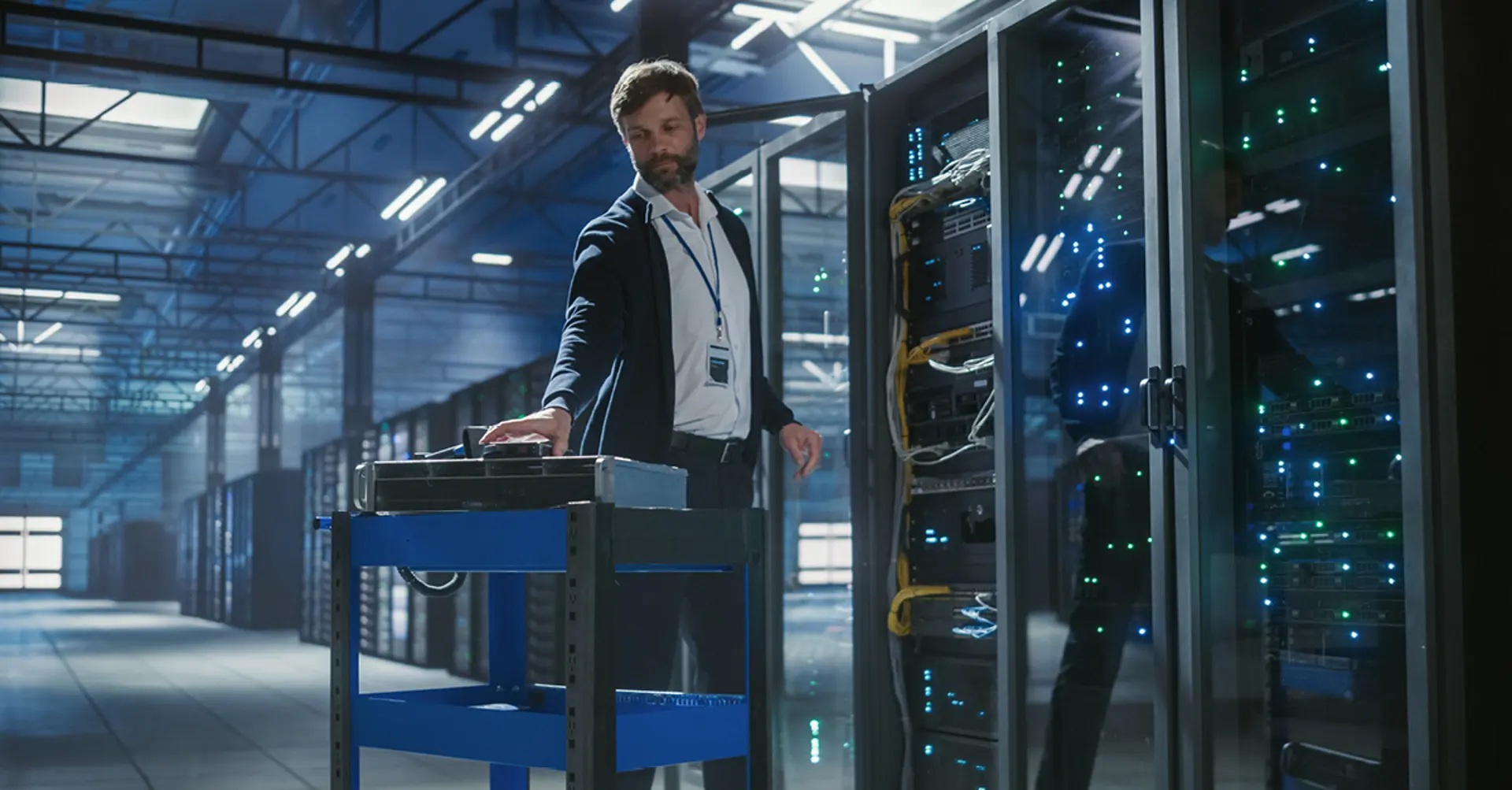 CBRE data center technician using a service cart to manage server rack equipment with illuminated networking hardware in a commercial facility.
